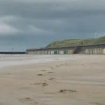 Plage du nord : sable mouillé, traces de pas, cabines et digue à marée basse